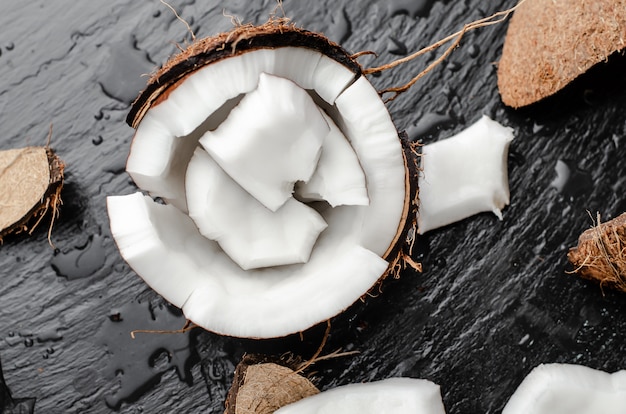 Coco orgánico hlf con piezas sobre fondo de piedra pizarra negra. Concepto de alimentos saludables altos en grasas.