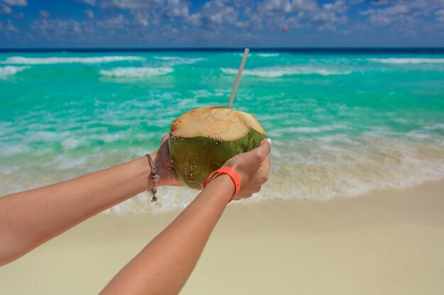 Foto coco con una paja en las manos sobre el fondo del mar