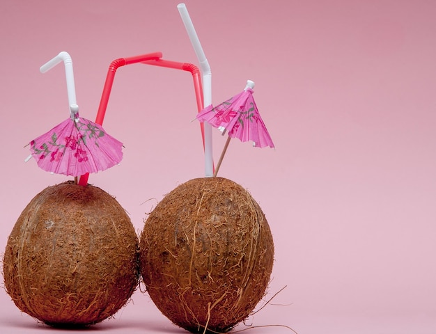 Coco con pajita y paraguas sobre fondo rosa