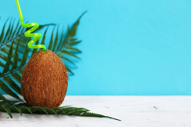 Un coco con pajita sobre un fondo azul.