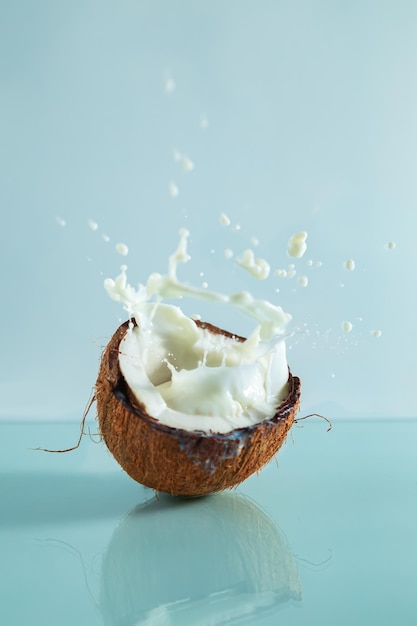 Coco roto y salpicaduras de leche de coco sobre un fondo azul