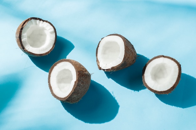 Coco roto en una superficie azul bajo luz natural con sombras. Luz dura. Concepto de dieta, alimentación saludable, descanso en los trópicos, vacaciones y viajes, vitaminas.