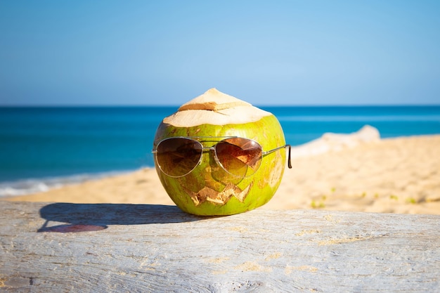 El coco verde fresco en gafas de sol es símbolo de Halloween se encuentra en un árbol con cara tallada como calabaza