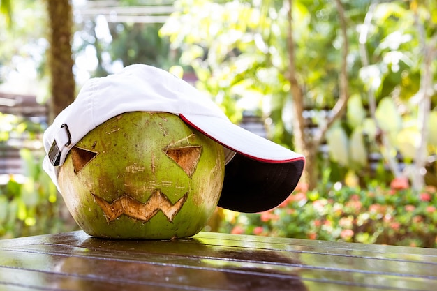 Coco verde fresco en la mesa con una gorra de béisbol blanca Símbolos de Halloween cara tallada de calabaza