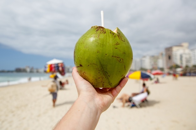 Coco verde fresco con una pajita sobre un fondo de playa.