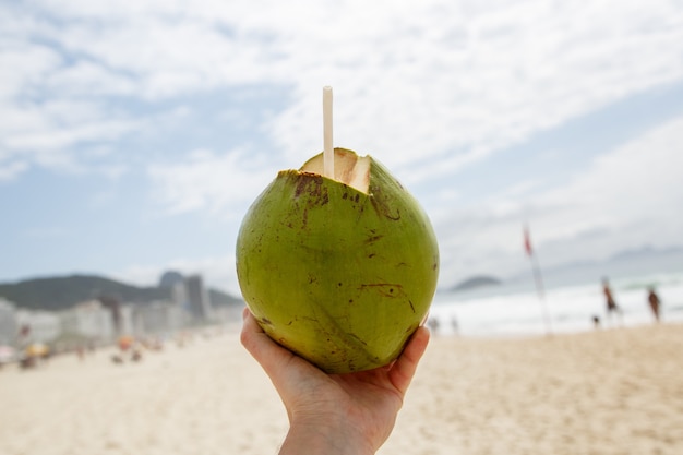 Coco verde fresco con una pajita sobre un fondo de playa.