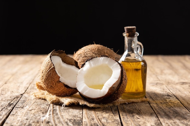 cocos fatiados com óleo dentro e garrafa de óleo de coco na mesa de madeira