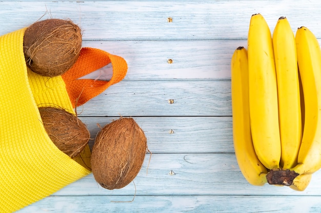 Cocos inteiros em um saco amarelo e bananas em um fundo azul de madeira