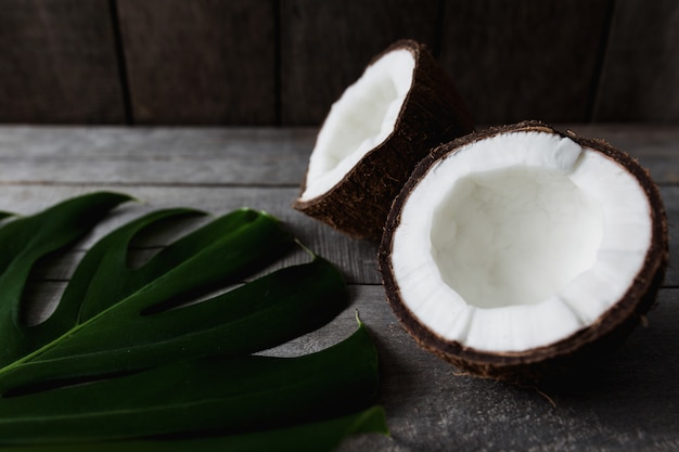 Cocos quebrados, fundo cinza de madeira, folha de palmeira monstera. polpa de coco branca. foto de alta qualidade