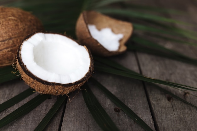 Cocos rotos en la superficie de madera gris con hoja de palma. Pulpa de coco blanco.