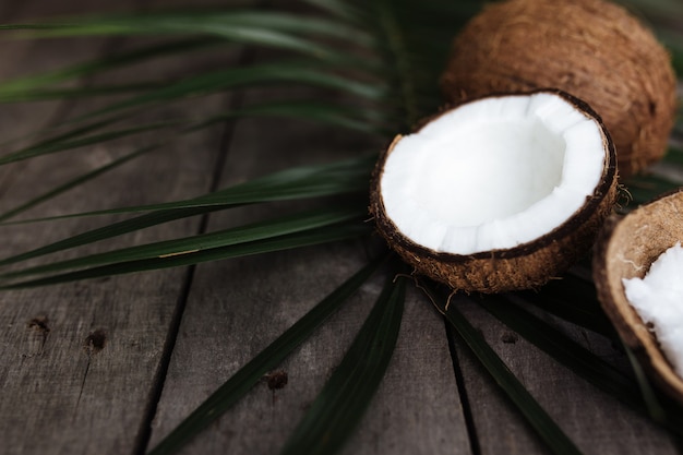 Cocos rotos en la superficie de madera gris con hoja de palma. Pulpa de coco blanco.