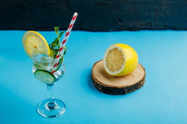 Foto coctel de agua de pepino con limón y menta en un vaso en una servilleta sobre un fondo azul cerca del limón