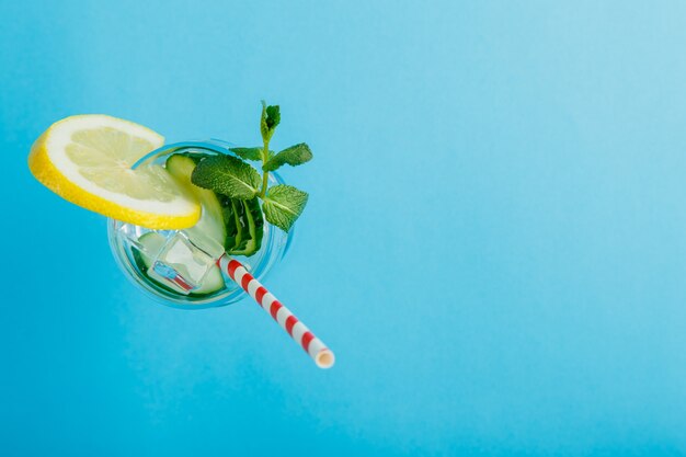 Cóctel de agua de pepino con limón y menta en un vaso sobre una servilleta sobre una superficie azul vista superior