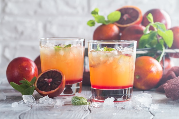 Cóctel de alcohol tequila sunrise con hielo rojo anaranjado y menta en blanco de madera