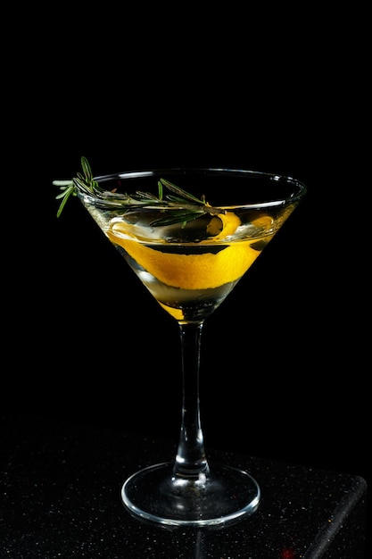 Cóctel de alcohol transparente Smoky Martini con ralladura de limón y romero sobre fondo negro