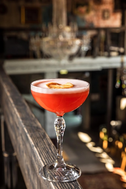 Un cóctel alcohólico agrio rosa con espuma adornado con rueda de limón seco servido en un vaso de copa en un restaurante o bar foto vertical