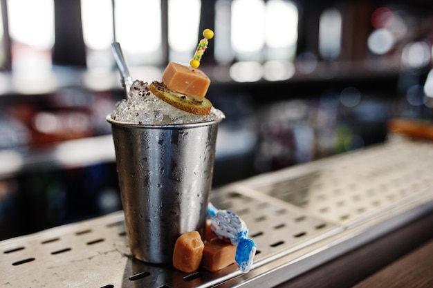 Cóctel alcohólico con dulces y caramelos en un pequeño cubo de plata en la mesa de bar