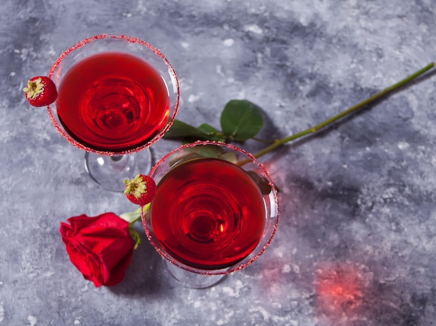 Cóctel alcohólico exótico rojo en vasos transparentes y rosa roja para una cena romántica.