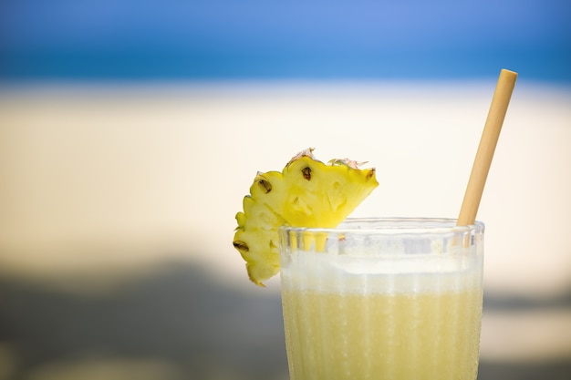 Cóctel alcohólico en vaso con rodaja de piña en la playa.