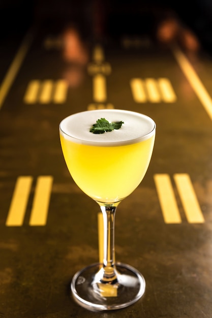 Un cóctel amarillo en un vaso de mella y nora adornado con cilantro en el bar.