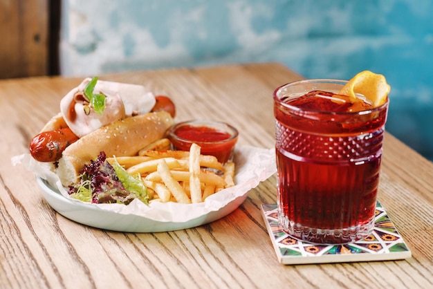 Cóctel a la antigua y plato con hot dog con salchicha y salsa de tomate con jamón ketchup