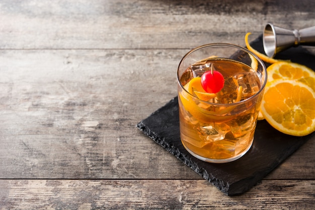 Cóctel antiguo con naranja y cereza en espacio de copia de mesa de madera