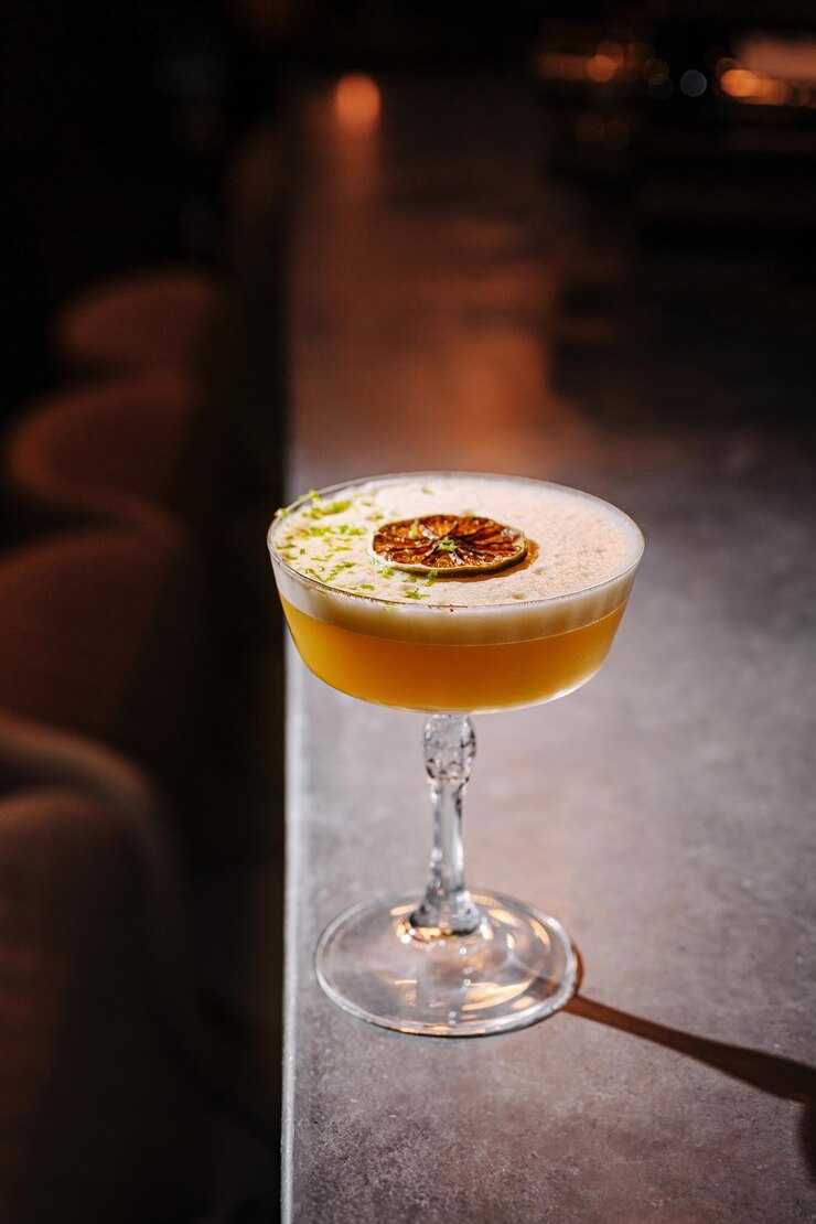 Un cóctel artesanal adornado con lima y cítricos servido en un elegante vaso en un mostrador de bar pulido