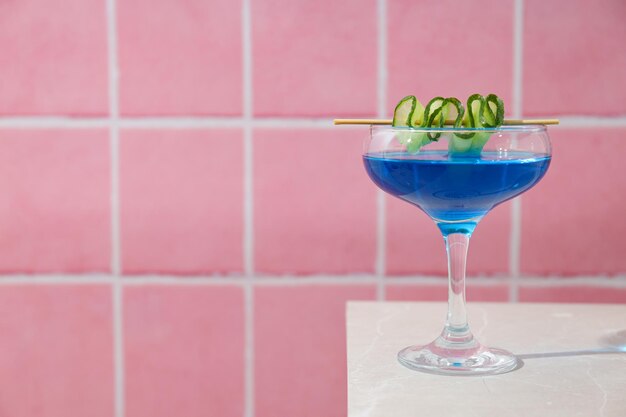 Cóctel azul con rebanada de pepino en vidrio sobre fondo rosa espacio para el texto