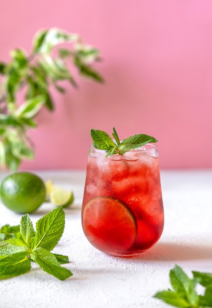 Cóctel de bayas con guarnición de menta y limón sobre fondo rosa