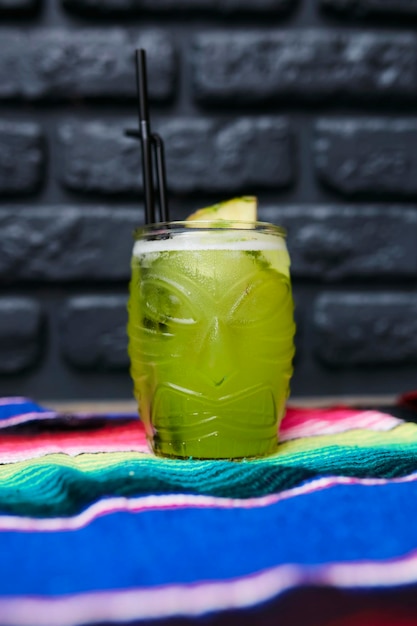 Foto cóctel de bichos de junio con un trozo de piña y lima sobre un fondo de pared de ladrillo negro