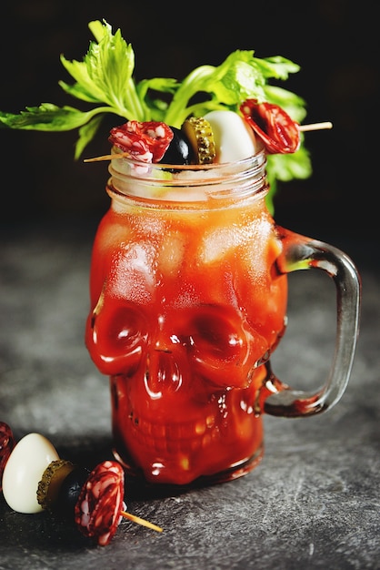 Cóctel Bloody Mary en calavera de cristal con palitos de apio, lima y verduras enlatadas