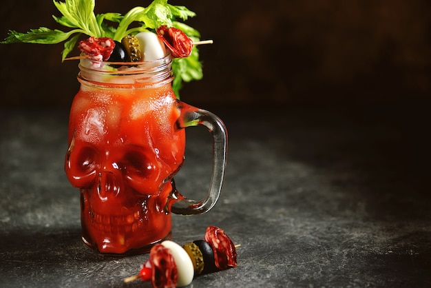 Cóctel Bloody Mary en calavera de cristal con palitos de apio, lima y verduras enlatadas