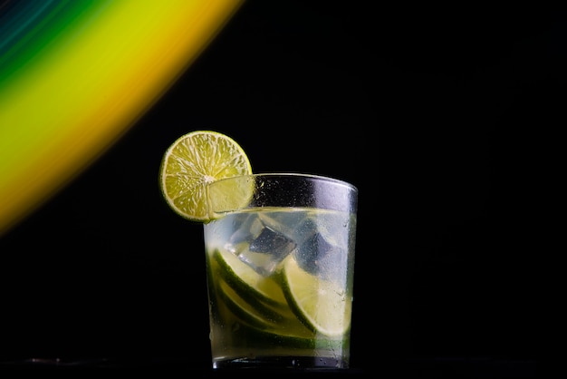 Cóctel brasileño llamado Caipirinha. Con limón, hielo y cachaÃ§a sobre un fondo oscuro con luces de colores. Copia espacio