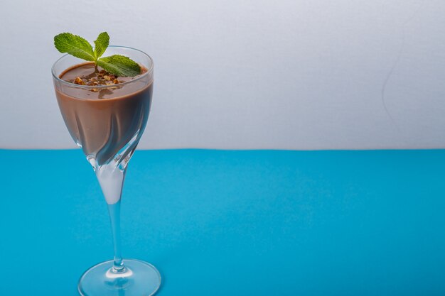 Cóctel de chocolate con nueces y menta en un vaso sobre un fondo azul. Foto horizontal