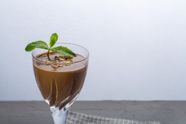 Cóctel de chocolate con nueces y menta en un vaso sobre una superficie azul sobre una servilleta