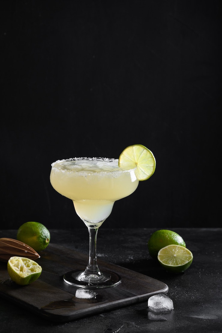 Foto cóctel clásico de margarita con jugo de limón y cubitos de hielo sobre fondo negro con orientación vertical
