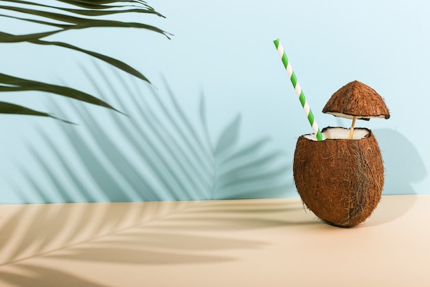 Cóctel en un coco abierto y la sombra de las hojas de palma en color. Humor de verano, cosecha.
