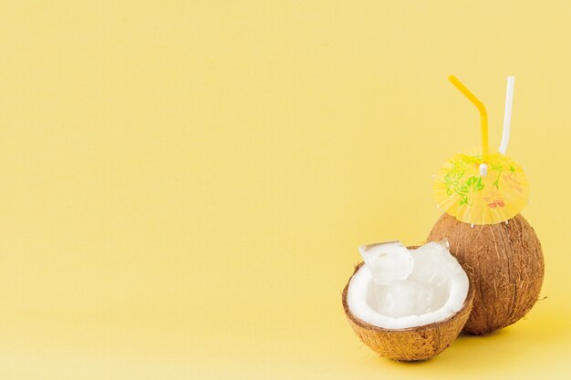 Cóctel de coco fresco con una pajita sobre fondo amarillo, espacio de copia