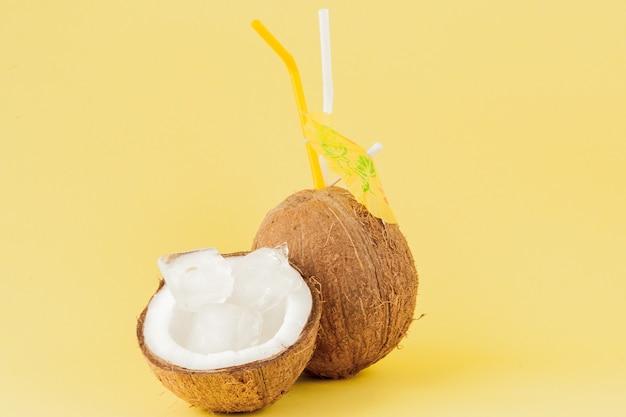 Cóctel de coco fresco con pajitas sobre fondo amarillo, espacio de copia