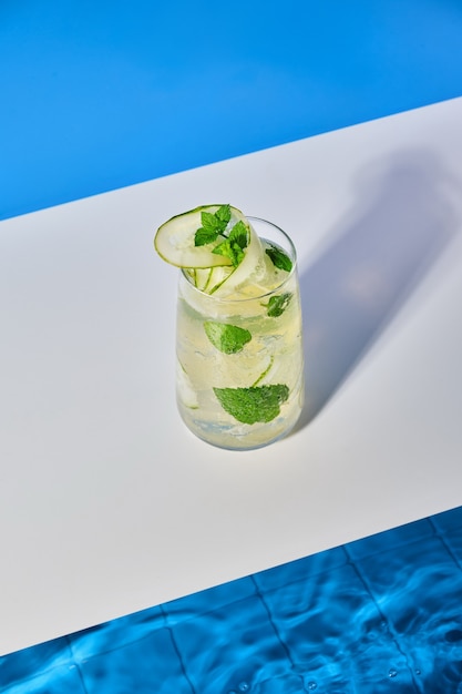 Cóctel fresco brillante con menta de pepino y cubitos de hielo junto a la piscina