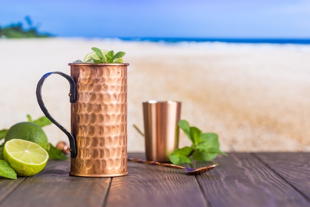 Cóctel frío de Moscow Mules con cerveza de jengibre, vodka y lima sobre la superficie de la playa y el mar