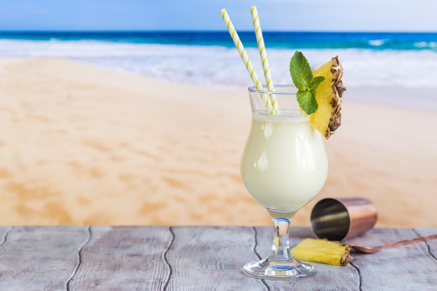 Cóctel frío de piña colada en un vaso en la playa con superficie marina