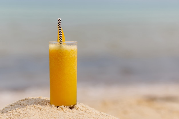 Foto cóctel de frutas múltiples frío con rodajas de mango en el fondo de la playa