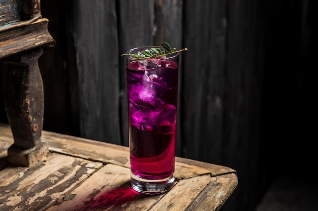 Cóctel de gin tonic hecho con ginebra morada servido con hielo en una copa de cóctel highball adornada con una foto horizontal de una ramita verde