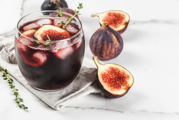 Cóctel helado de otoño con vino tinto, tomillo e higos, en mesa de mármol blanco,