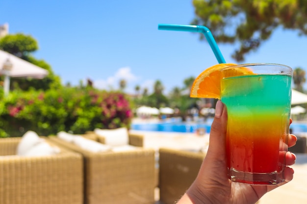 Cóctel de hielo tropical jugoso colorido fresco en la mano de la mujer cerca de la piscina.