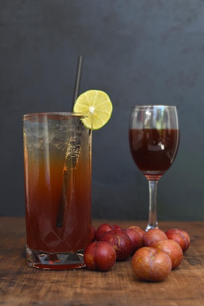 Cóctel de highball de vino de ciruela con una copa de vino y ciruelas sobre una mesa de madera y fondo negro