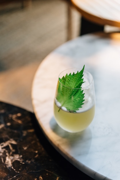 Cóctel japonés Yuzu con hojas de shiso (perilla verde) en vidrio sobre mesa de mármol.