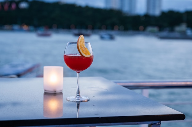 Cóctel de jugo de naranja en copa de vino y lámpara en la mesa en el mar