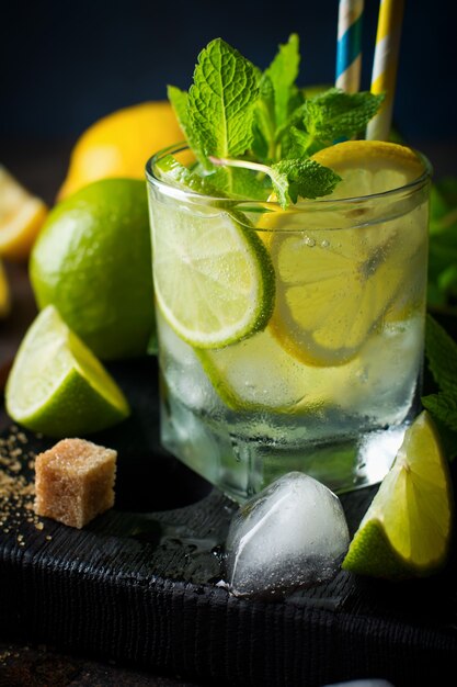 Cóctel de mojito en vaso con limón, menta fresca y hielo sobre un fondo oscuro.